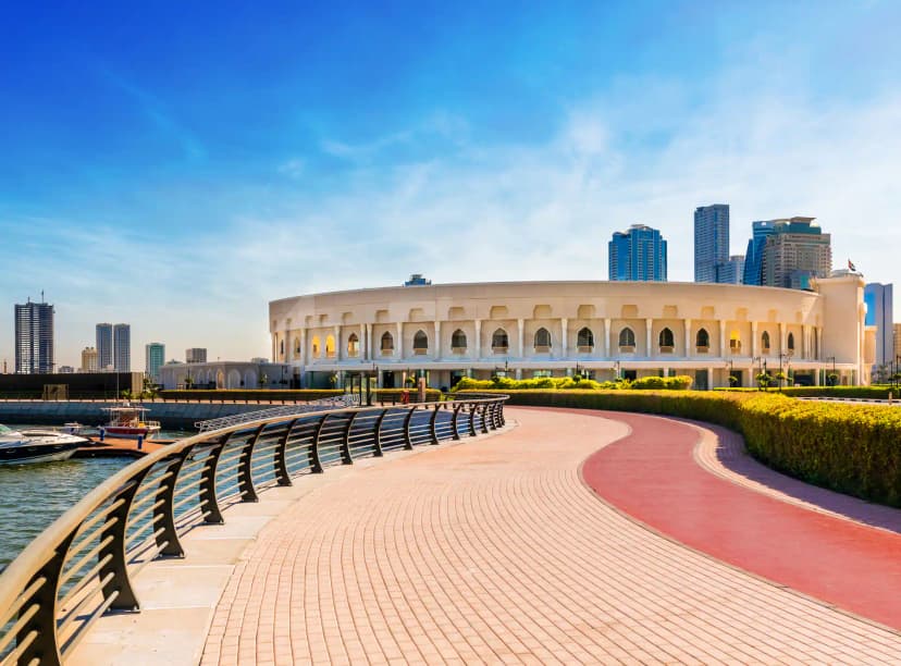 AlMajaz Amphitheatre Sharjah circular beige building with arched windows and white columns, viewed from a curved brick pathway