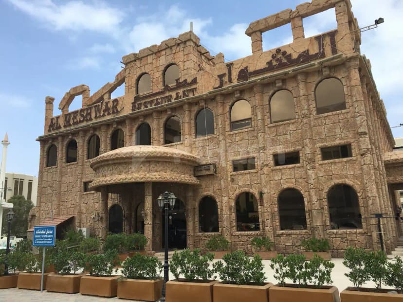 Hotel facade of Al Meshwar Restaurant Dubai featuring a stone exterior with arched windows and an ornate entrance