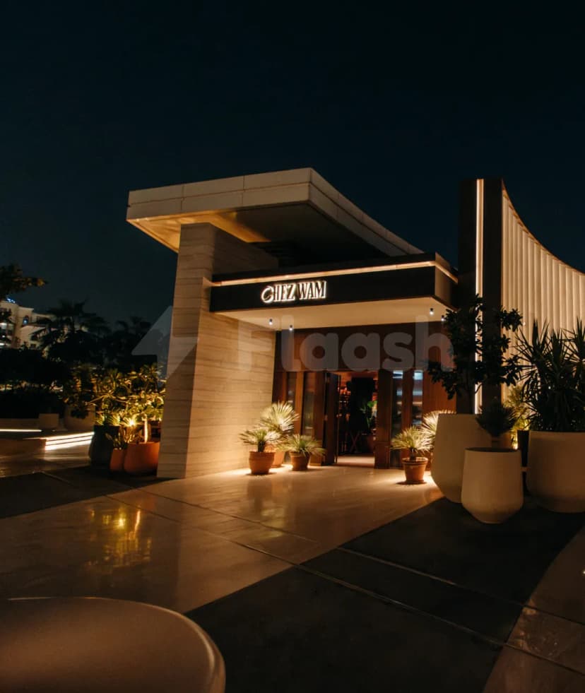 Entrance hall of Chez Wam in Dubai at night, featuring an illuminated sign, stone pillar, and potted plants