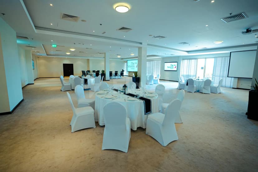 Ballroom at The Sevens Stadium in Dubai set with round tables, white chair covers, and digital screens displaying