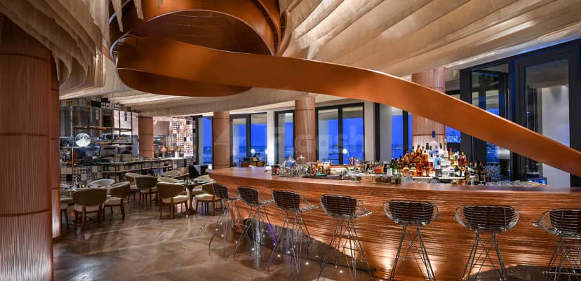 Bar counter at B Lounge Doha with a prominent hanging copper sculpture and large windows overlooking the ocean