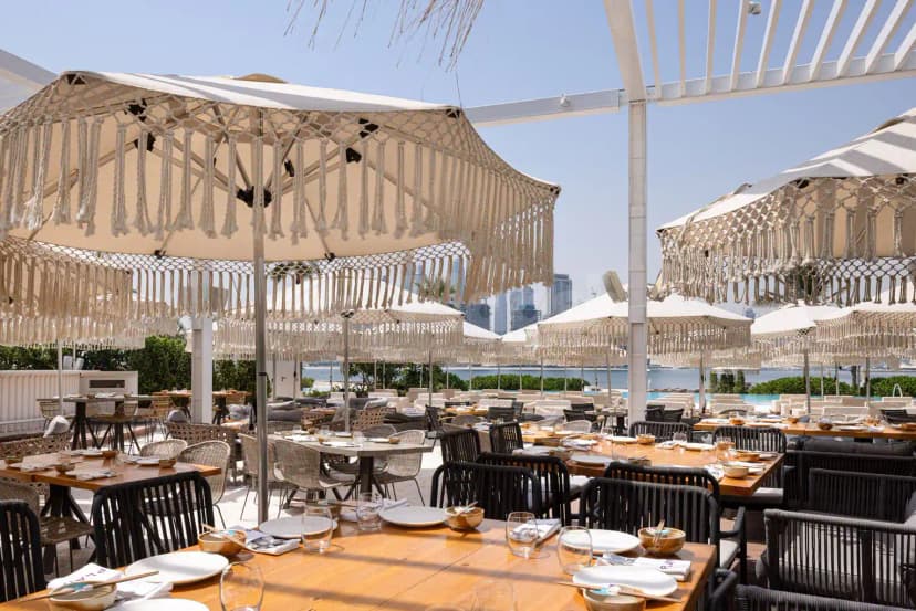 Rooftop terrace at Playa Dubai featuring beige macrame umbrellas and a white pergola structure with waterfront and city