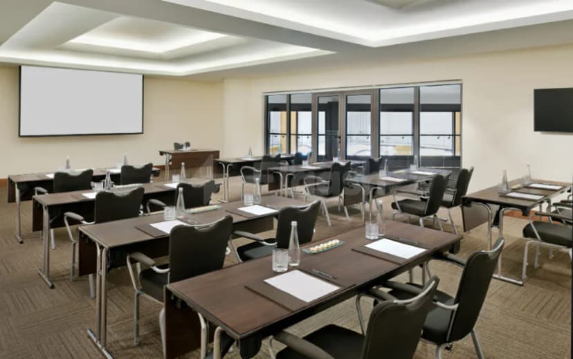 Meeting room at JA Ocean View Hotel Dubai with rectangular tables, black chairs, and a large projection screen