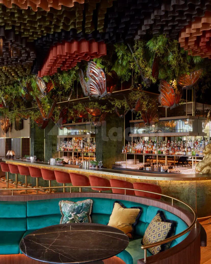 Bar counter at Amazónico Dubai featuring decorative butterfly sculptures and hanging green plants under a layered fabric