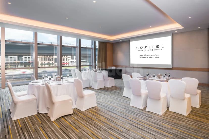 Meeting room at Sofitel Dubai Downtown with round tables, white chair covers, and a projector screen displaying