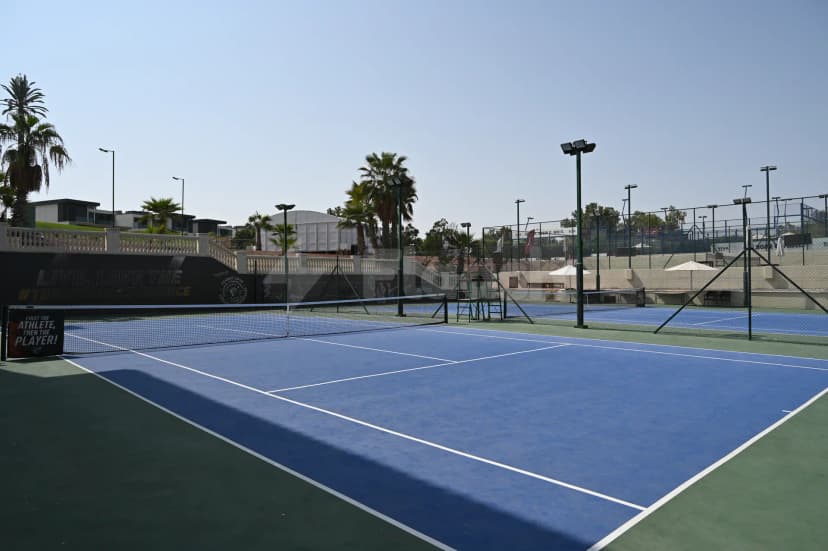 Blue tennis court at Jumeirah Golf Estates in Dubai, featuring a black banner with text and palm trees