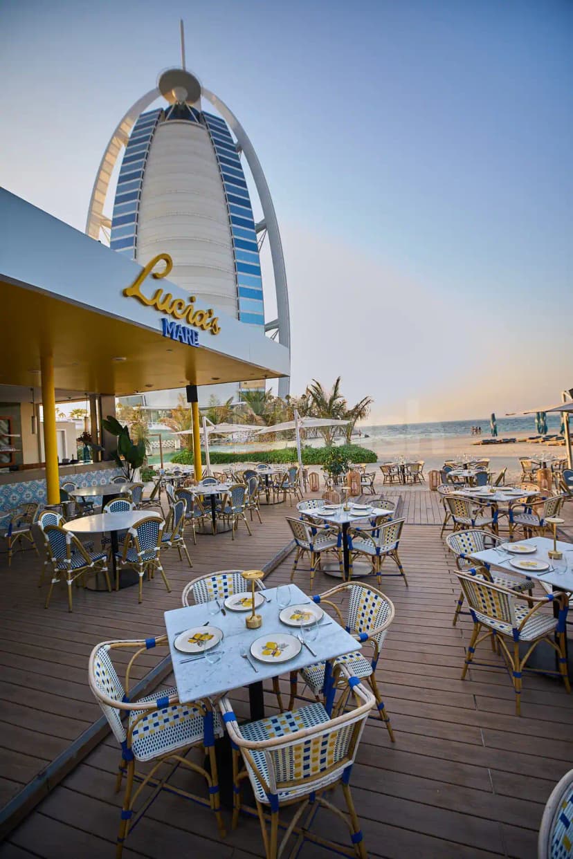 Terrace at Lucia's Mare Restaurant Dubai with wooden deck, patterned wicker chairs, marble tables, and Burj Al Arab