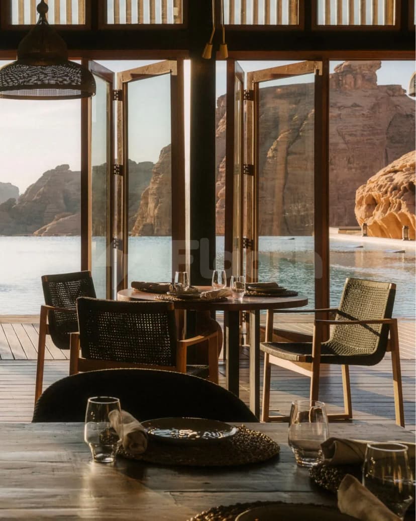 Restaurant at Tama At Habitas AlUla with round wooden table, woven chairs, and open glass doors framing desert