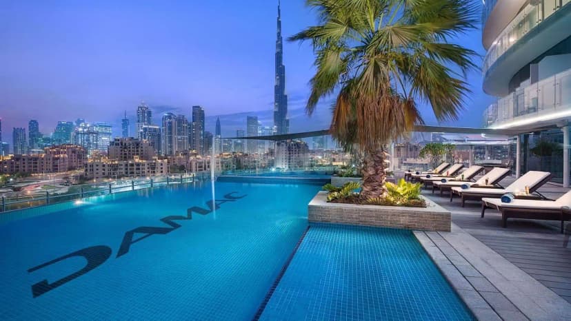 Rooftop pool at Blooms Ava Restaurant in Dubai with DAMAC logo on blue tiles, palm tree, and Burj