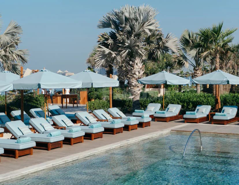 Rectangular swimming pool at La Cantine Beach in Dubai, surrounded by wooden sun loungers and palm trees under