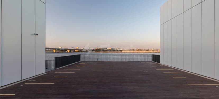 Rooftop terrace at Jameel Arts Centre Dubai with wooden deck, white panelled walls, black railing, and river view
