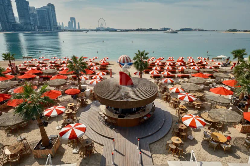 Circular thatched bar at February 30 in Dubai, set on a sandy terrace with palm trees and waterfront