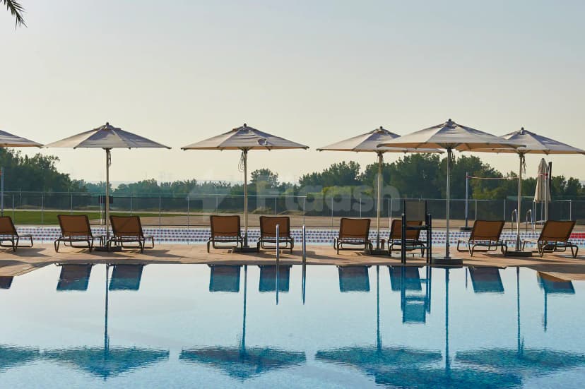 Rectangular swimming pool at Jumeirah Golf Estates Dubai with calm blue water reflecting large white umbrellas and lounge