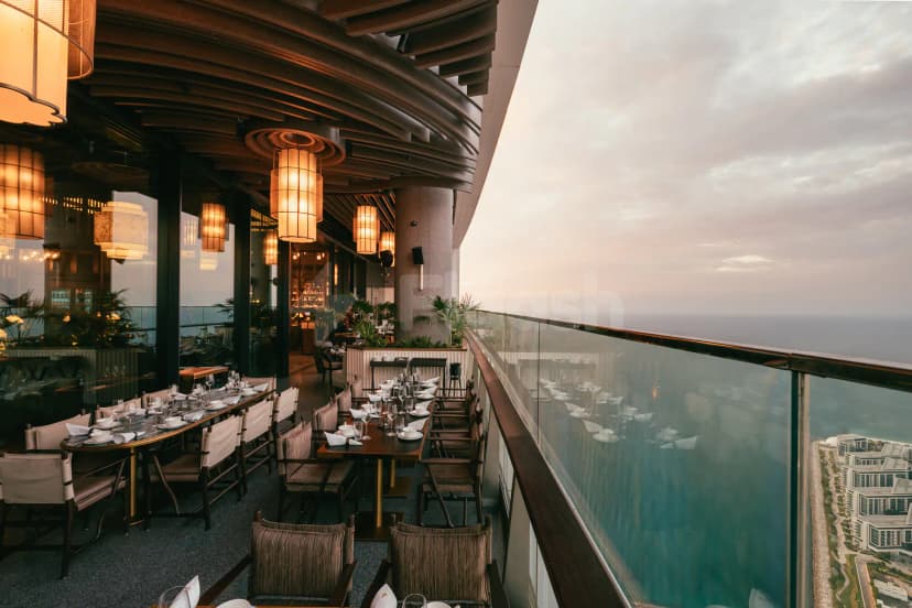 Rooftop terrace at Mott 32 Dubai featuring wooden ceiling beams, pendant lighting, and a glass railing overlooking