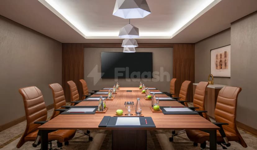 Boardroom at Swissotel Living Jeddah featuring a long wooden table, brown leather chairs, a wall-mounted screen, and geometric