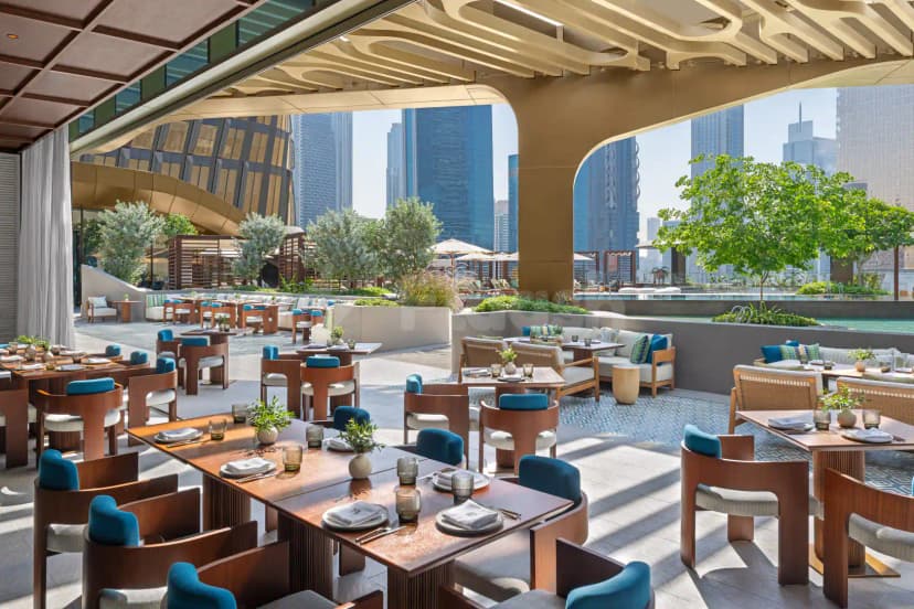 Rooftop terrace at Mandarin Oriental Downtown Dubai featuring wooden tables, blue upholstered chairs, and a city skyline view