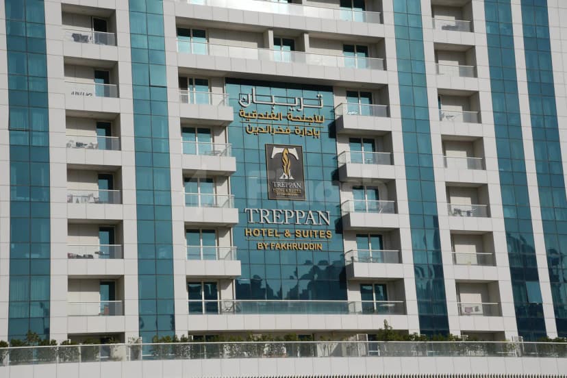 Hotel facade of Treppan Hotel & Suites in Dubai featuring blue-tinted glass panels, white concrete cladding, and recessed balconies