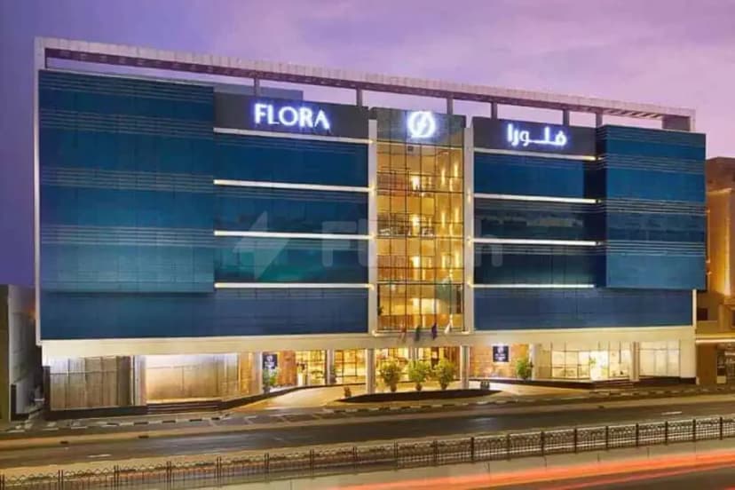 Hotel facade of Flora Inn Hotel Dubai Airport at dusk, featuring blue glass panels and illuminated FLORA signage