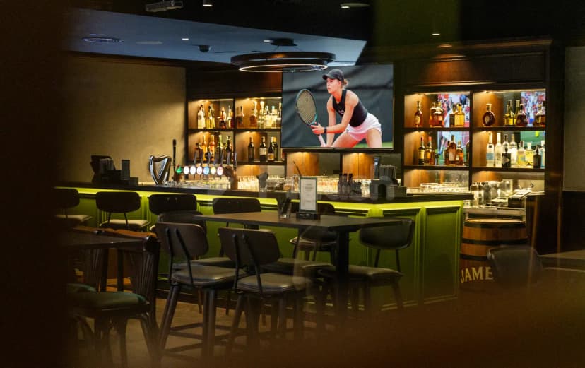 Restaurant at Five Iron Golf Dubai featuring a bar counter with backlit shelves and a large screen TV