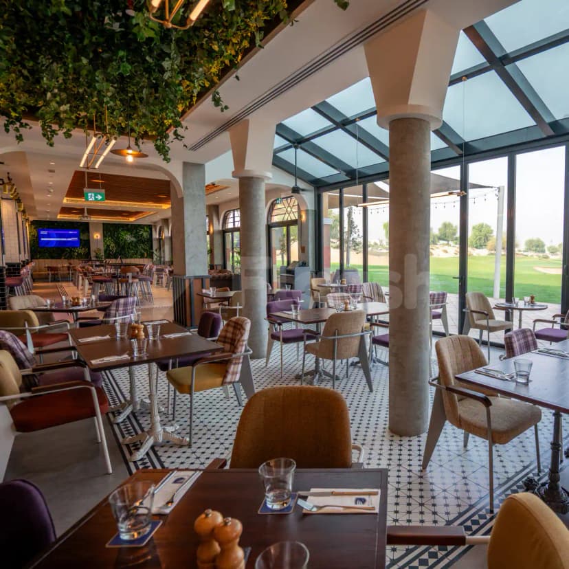 Restaurant at The Els Club Dubai Sports City featuring concrete pillars, a glass ceiling, and large windows overlooking
