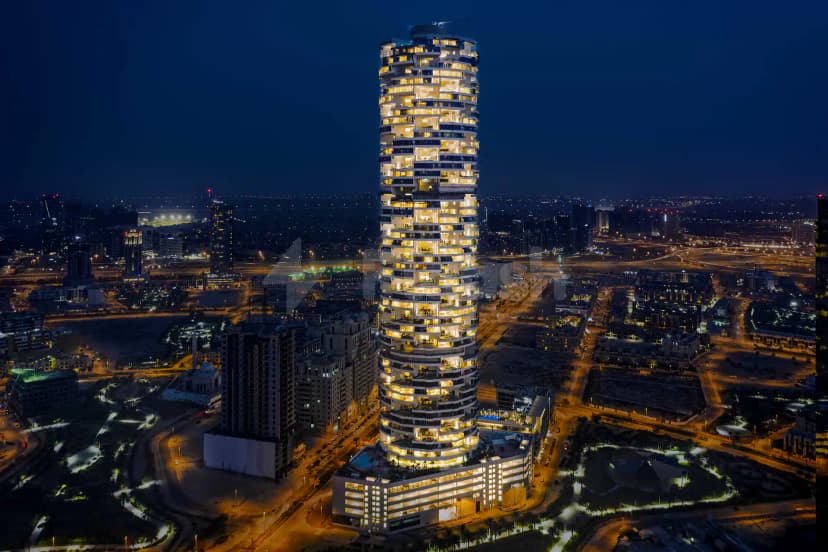 Tall curved skyscraper facade of Five Jumeirah Village in Dubai, illuminated windows and circular balconies visible against