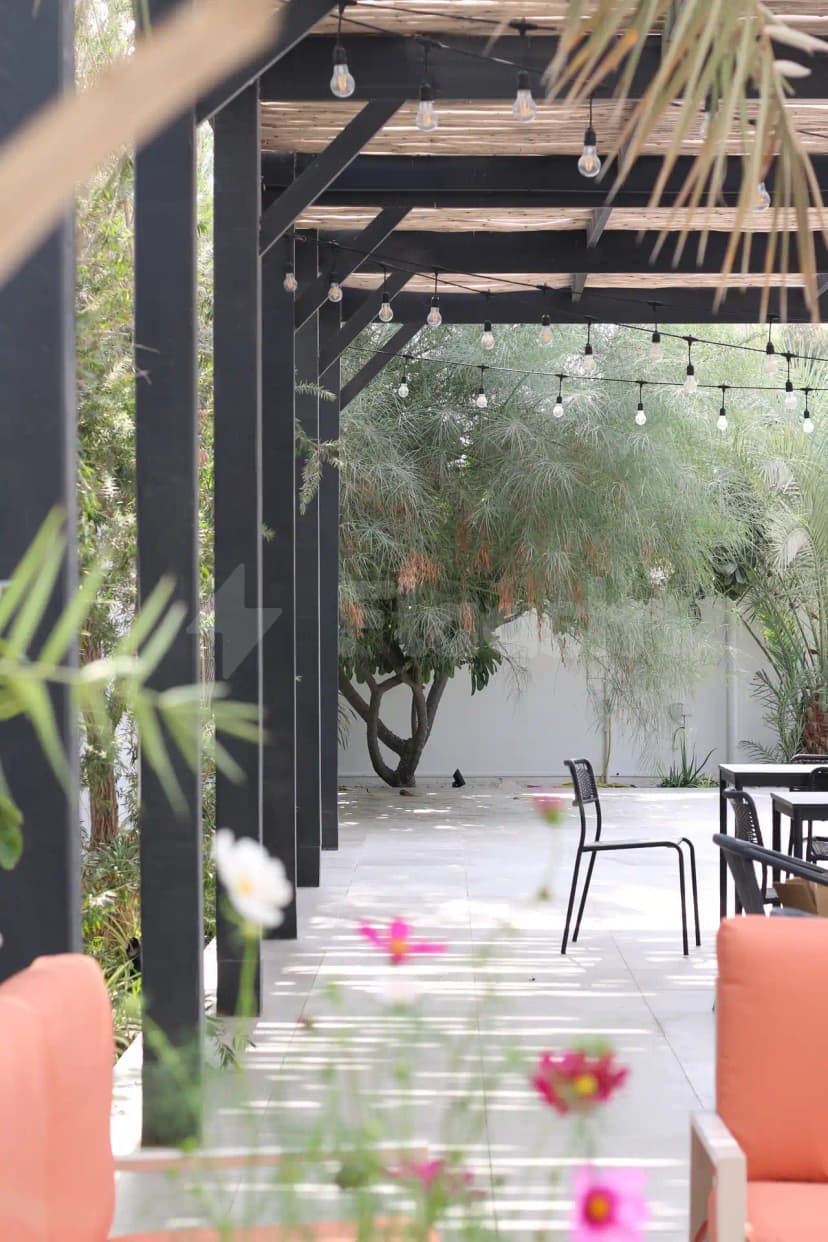 Terrace at Tania's Teahouse Dubai Hills featuring a black metal pergola with wooden slats and hanging Edison bulbs