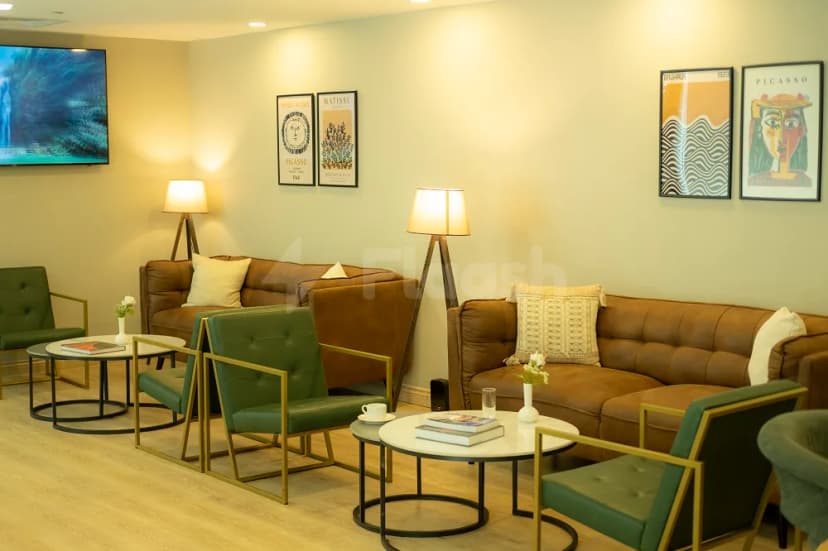 Meeting room at Momento Lounge Doha featuring brown leather sofas, green velvet armchairs with gold frames, and framed