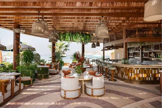 Rooftop terrace at Baoli Restaurant Dubai featuring a thatched roof, wooden pillars, hanging pendant lights, and an ocean