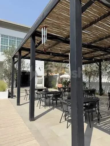 Rooftop terrace at Keyani Wellness in Dubai featuring a black metal pergola with woven thatch roof and wooden