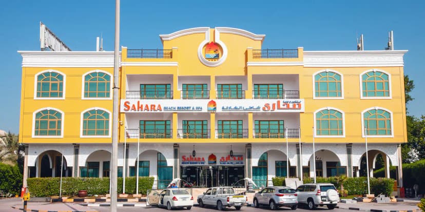 Hotel facade of Sahara Beach Resort & Spa in Sharjah featuring arched windows, white decorative trim, and entrance arches