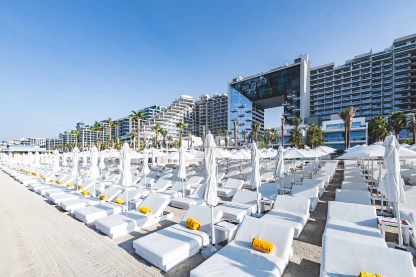 Beach By Five Beach Party Dubai outdoor seating area with white sun loungers, yellow towels, and modern high-rise