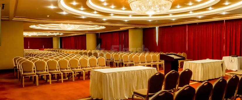 Ballroom at Excelsior Hotel Downtown Dubai featuring rows of beige chairs, a black podium, red curtain backdrop