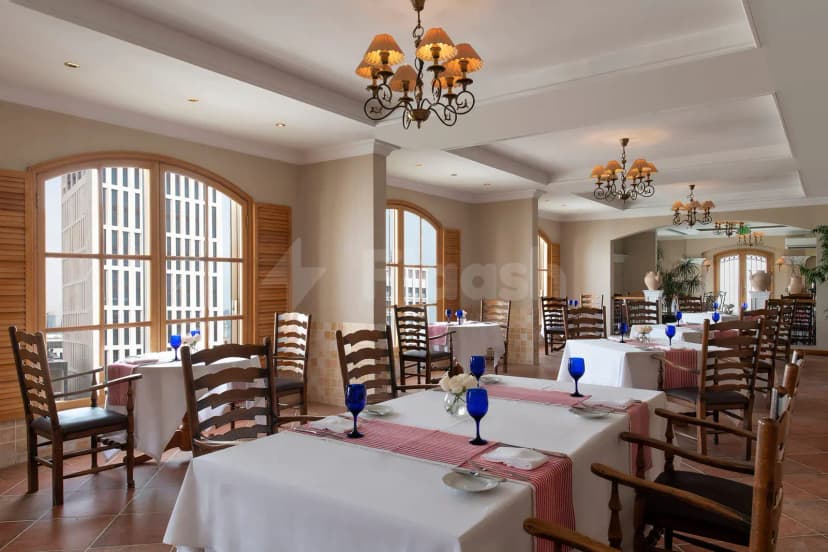 Restaurant at Treffen House Doha featuring arched windows with wooden shutters and chandeliers with fabric shades over set