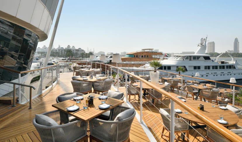 Rooftop terrace at Dubai Creek Golf & Yacht Club in Dubai with wooden deck, wicker chairs, and yachts docked