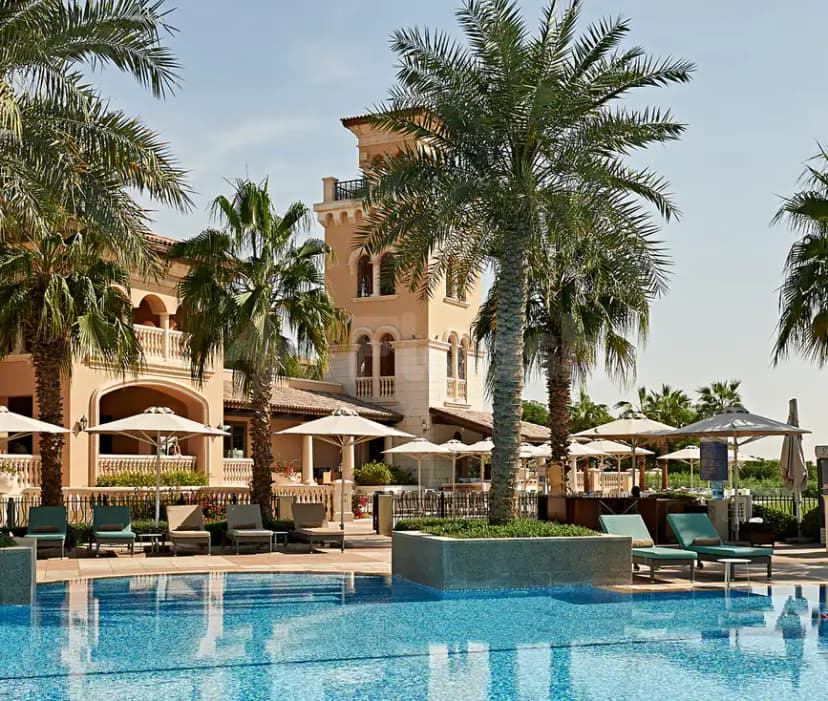 Rectangular swimming pool at Jumeirah Golf Estates in Dubai, surrounded by tall palm trees and a beige stucco