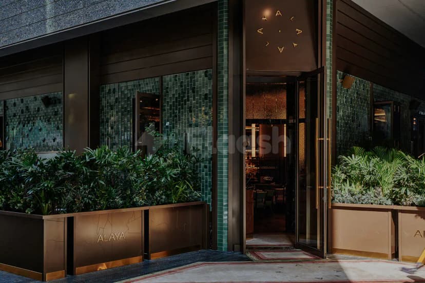 Entrance hall of Alaya Dubai featuring glass double doors, green tile walls, and bronze planters with tropical foliage