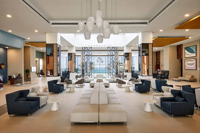 Entrance hall at Hotel Riu Dubai featuring high ceilings with white pendant lighting and a glass wall offering