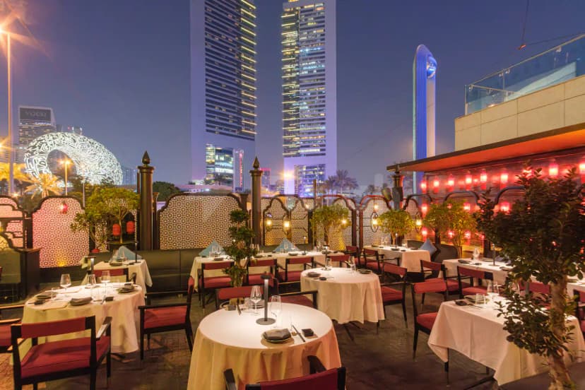 Rooftop terrace at Hutong Dubai featuring round tables with white linens, red chairs, decorative lattice screens