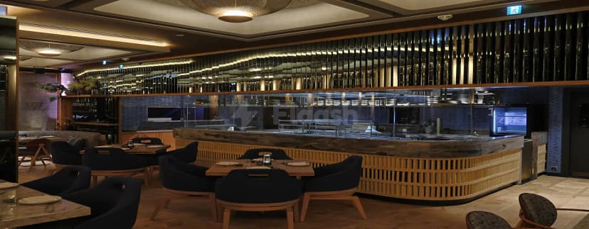 Open kitchen with glass partition and wooden counter at Robata Riyadh, featuring slatted wood paneling and dark blue