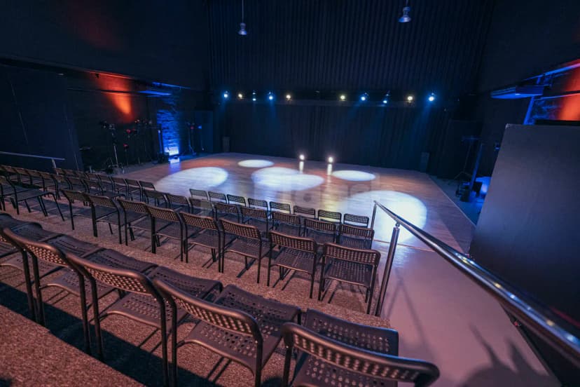 Sima Performing Arts Dubai ballroom with wooden stage, black perforated metal chairs, and circular spotlight patterns on floor