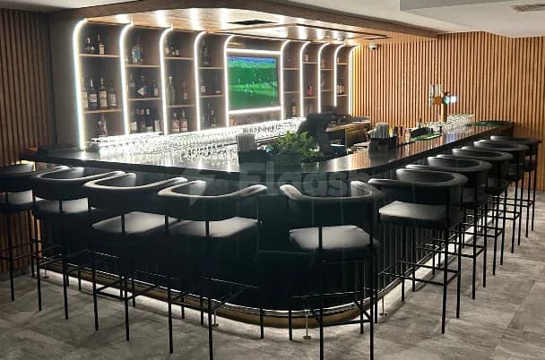 Bar counter at Five Iron Golf Dubai featuring backlit shelving with bottles and a television screen