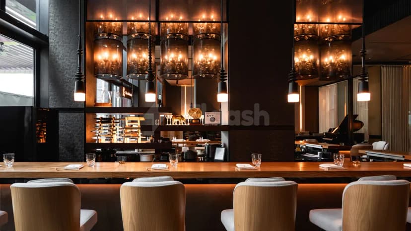 Long wooden bar counter at TakaHisa Restaurant Dubai with hanging cylindrical pendant lights and dark textured walls