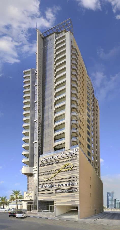 Hotel facade of Al Majaz Premiere Hotel Apartments in Sharjah, featuring curved balconies and a striped stone wall