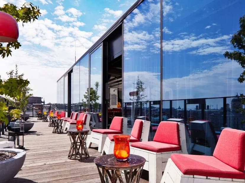 Rooftop terrace at Ernst Biergarten Restaurant Dubai featuring wooden decking, red cushioned chairs, and a glass wall reflecting