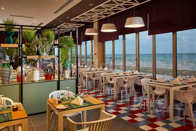 Restaurant at Hotel Riu Dubai with large ocean-facing windows and a red-and-white checkered floor
