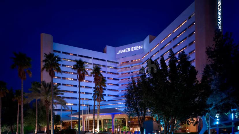 Hotel facade of Le Meridien Al Khobar at night, featuring illuminated signage, palm trees, and a glass entrance