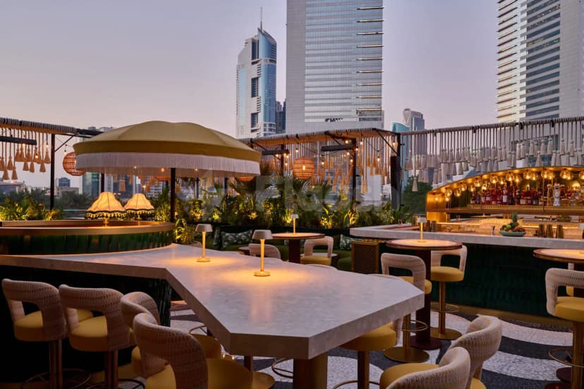Rooftop terrace at Amazónico Dubai featuring a large yellow umbrella with white fringe and woven pendant lights