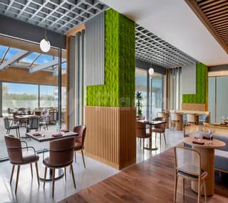 Modern restaurant interior at Swissotel Living Jeddah featuring a green living wall and vertical wood paneling with natural