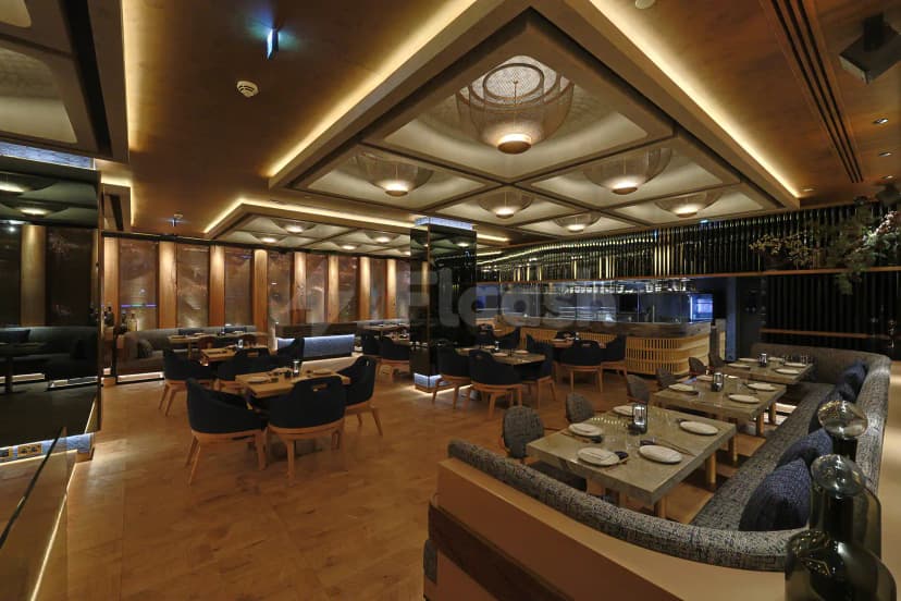 Restaurant interior at Robata Riyadh featuring wooden herringbone flooring, woven pendant lights, and an open kitchen visible behind
