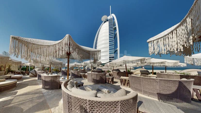 Terrace at Verde Beach Restaurant Dubai featuring white macrame canopy umbrellas and woven wicker lounge chairs with Burj